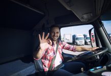 Truck driver loving his job and showing okay gesture sign while sitting in his truck cabin. Transportation services.