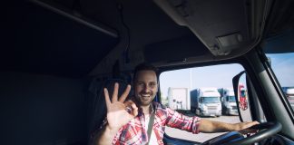 Truck driver loving his job and showing okay gesture sign while sitting in his truck cabin. Transportation services.
