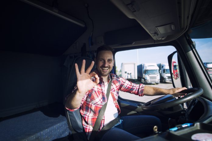 Truck driver loving his job and showing okay gesture sign while sitting in his truck cabin. Transportation services.