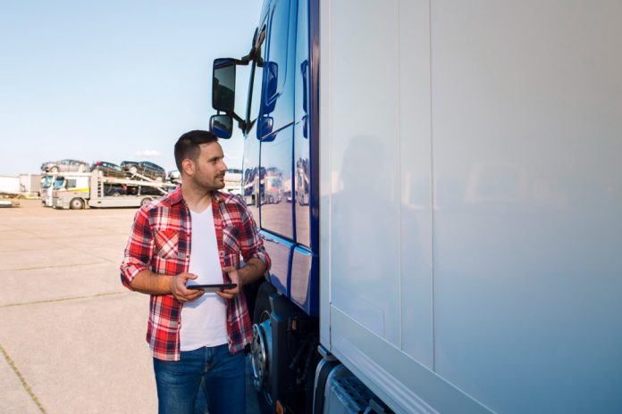 truck-driver-casual-clothes-standing-by-his-truck-with-tablet-looking-truck