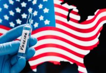 Hand in rubber medical gloves holding vaccine against coronavirus, USA flag in background