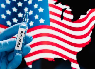 Hand in rubber medical gloves holding vaccine against coronavirus, USA flag in background