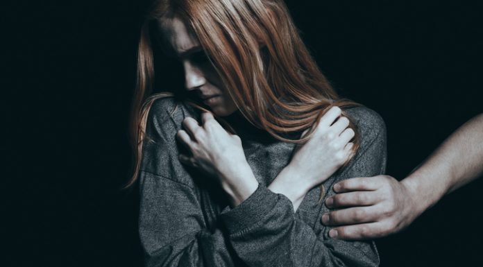 Fearful rape victim, man holding her arm, black background