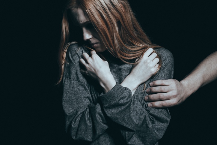 Fearful rape victim, man holding her arm, black background