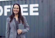 Portrait Of Female Freight Haulage Team Manager Standing By Shipping Container With Digital Tablet