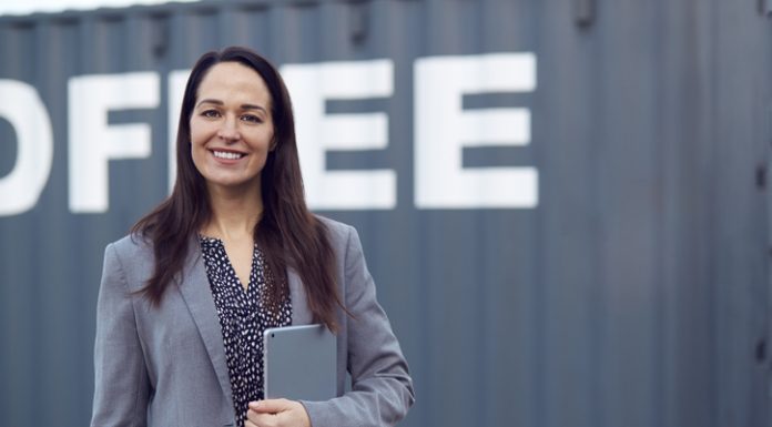 Portrait Of Female Freight Haulage Team Manager Standing By Shipping Container With Digital Tablet