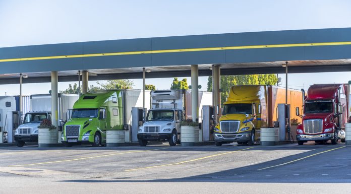 Different big rigs long and local haul semi trucks standing under the eaves on the truck stop fuel station for refueling and continuation of the cargo delivery route according to the schedule