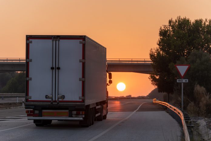 Truck with refrigerated semi-trailer driving on the highway with the sun in front of it at sunset.