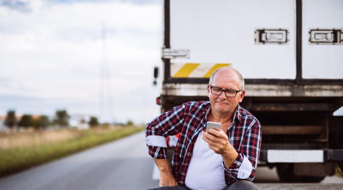 Senior truck driver checking his mobile phone. sitting behind his truck.