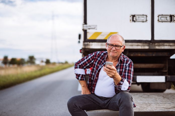 Senior truck driver checking his mobile phone. sitting behind his truck.