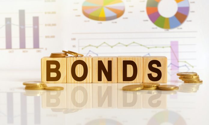 Bonds the word on wooden cubes, cubes stand on a reflective surface, in the background is a business diagram. Business and finance concept