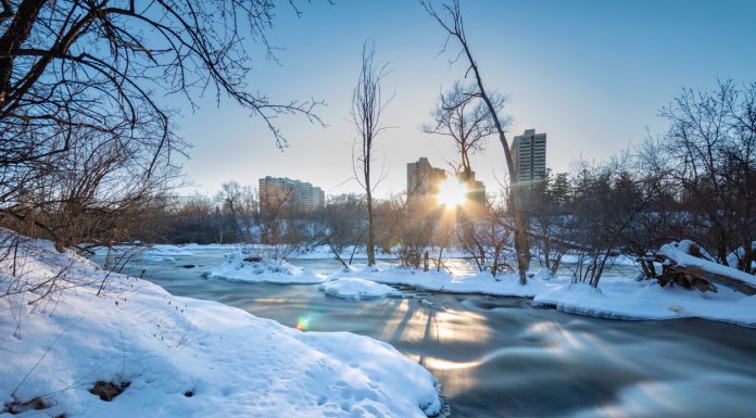 A long exposure photo of rapids in winter with the sun low in the sky, taken in Canada