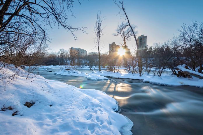 A long exposure photo of rapids in winter with the sun low in the sky, taken in Canada