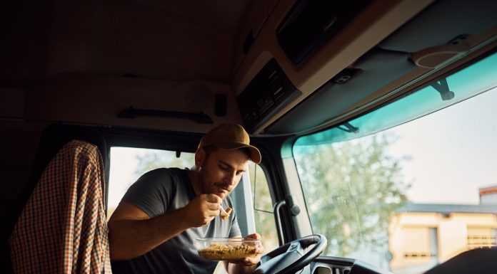 Male driver eating while making lunch break in truck's cabin.
